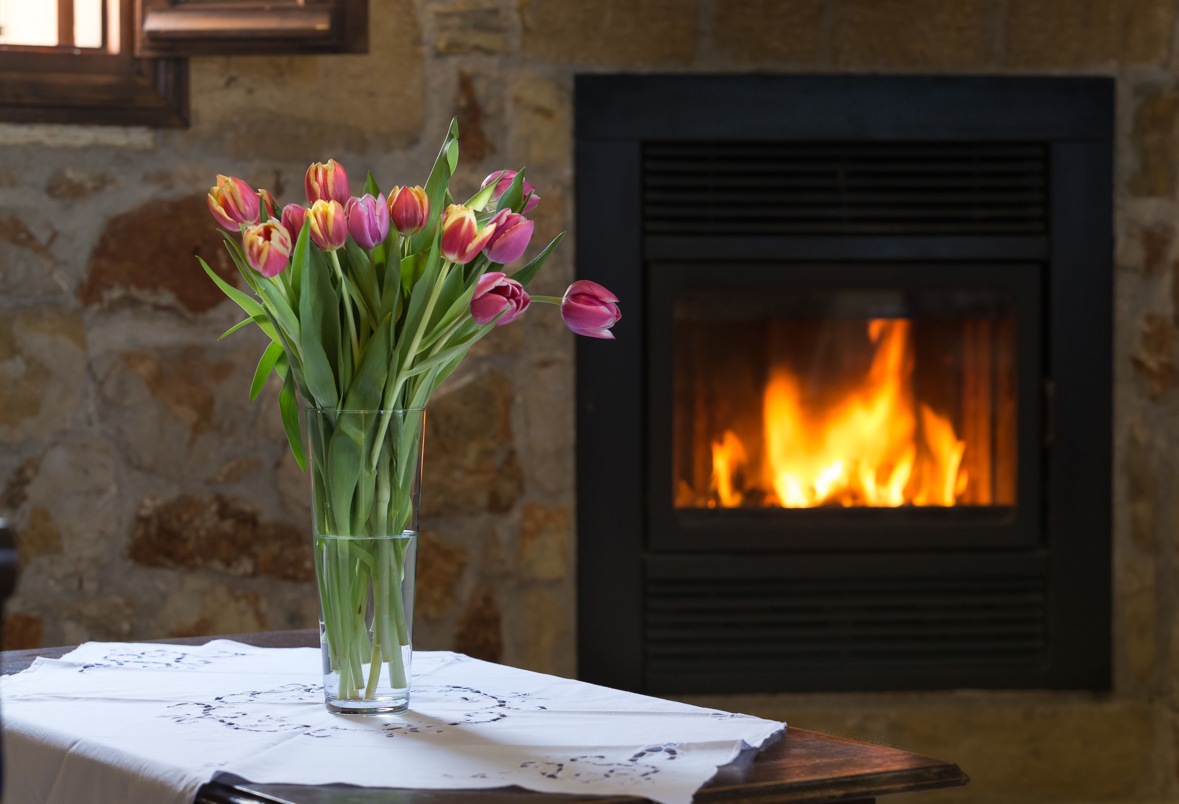 Een vaas met tulpen op een tafel voor een open haard.