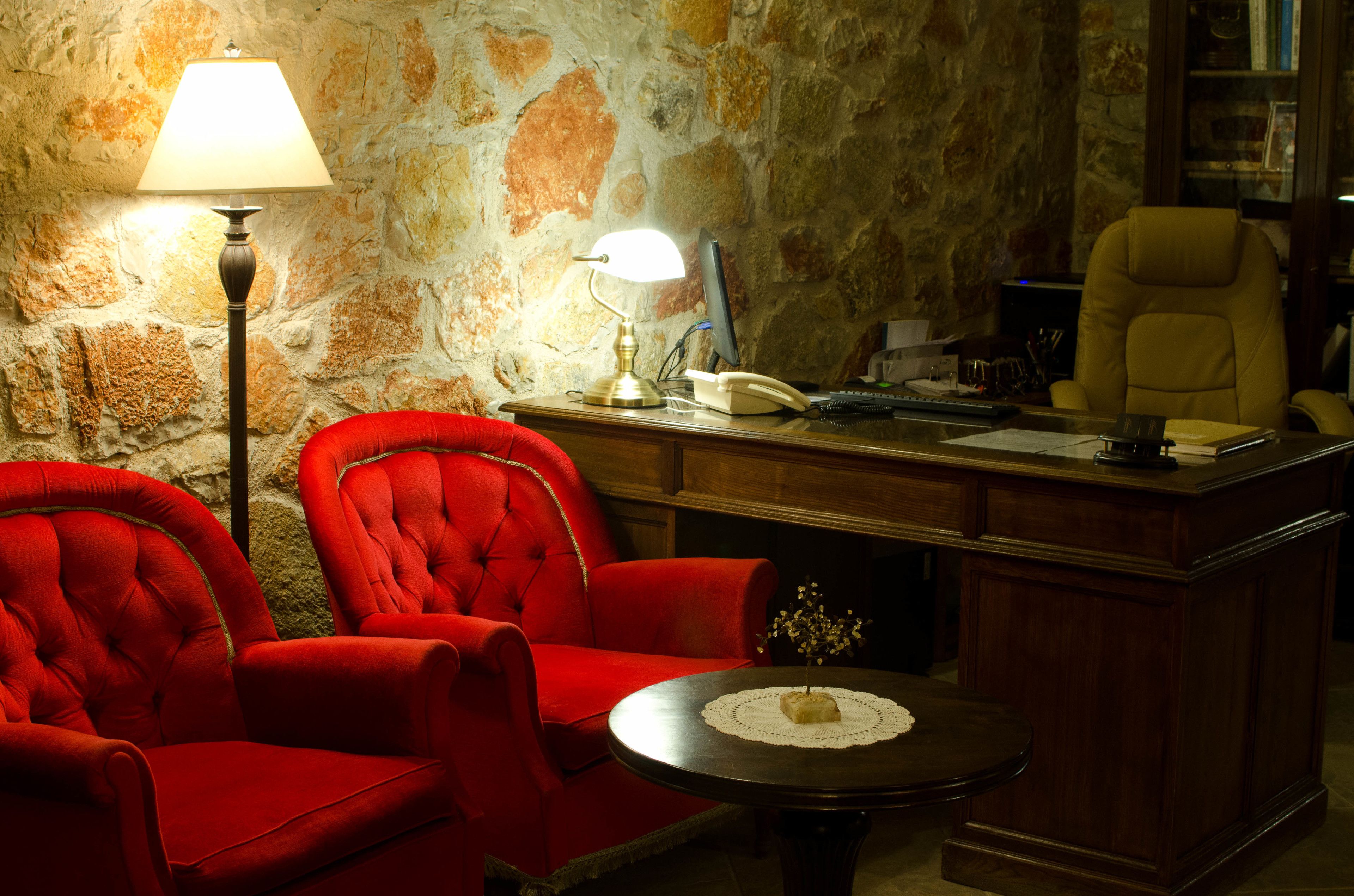 A room with a stone wall, a desk with a telephone, a lamp, and two red chairs.
