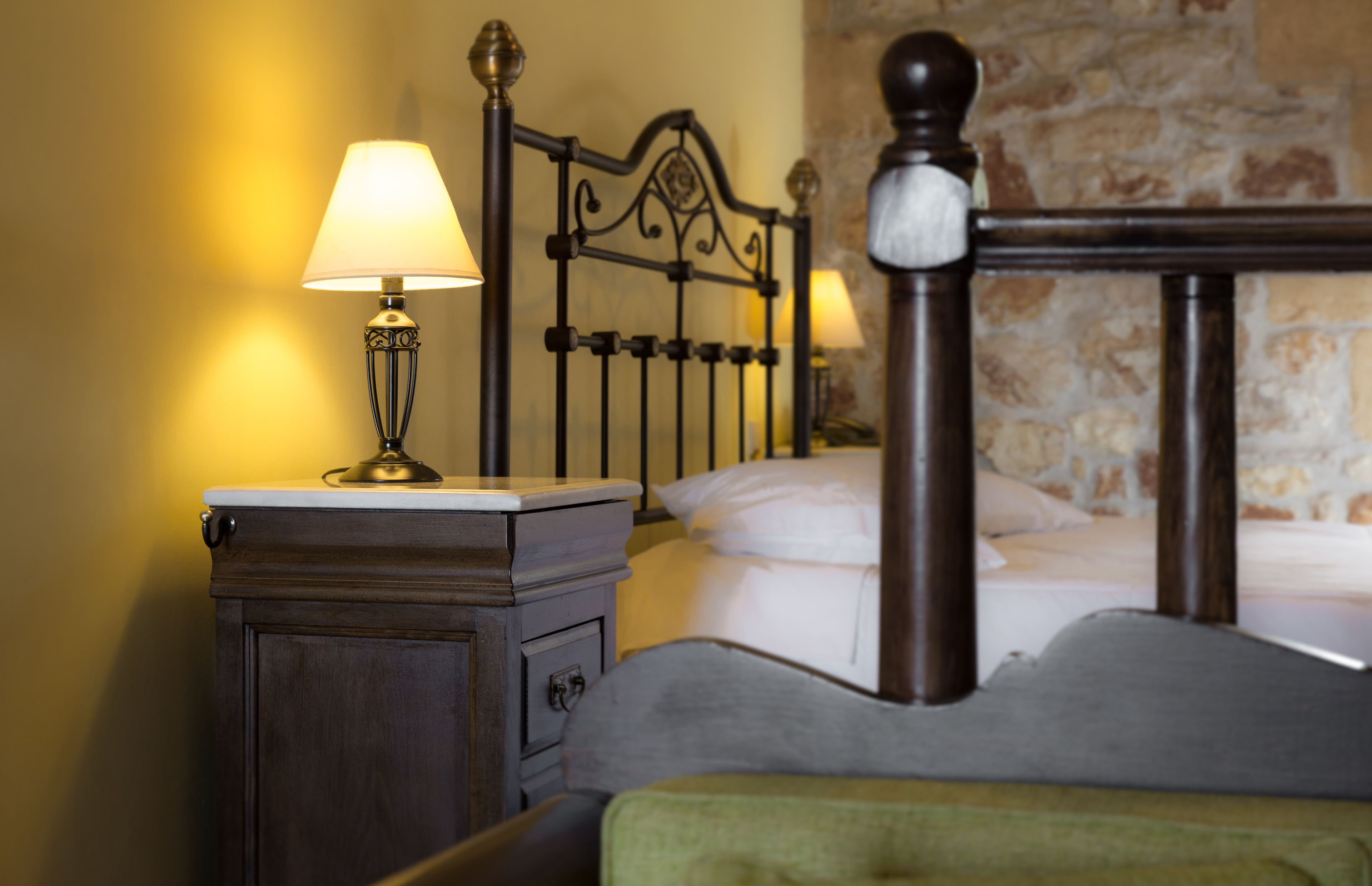 A neatly made bed with a headboard, a bedside table with a lamp, and a nightstand.