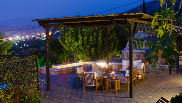 Área de pátio externa com móveis de madeira e uma pérgola, com vista para o horizonte urbano à noite.