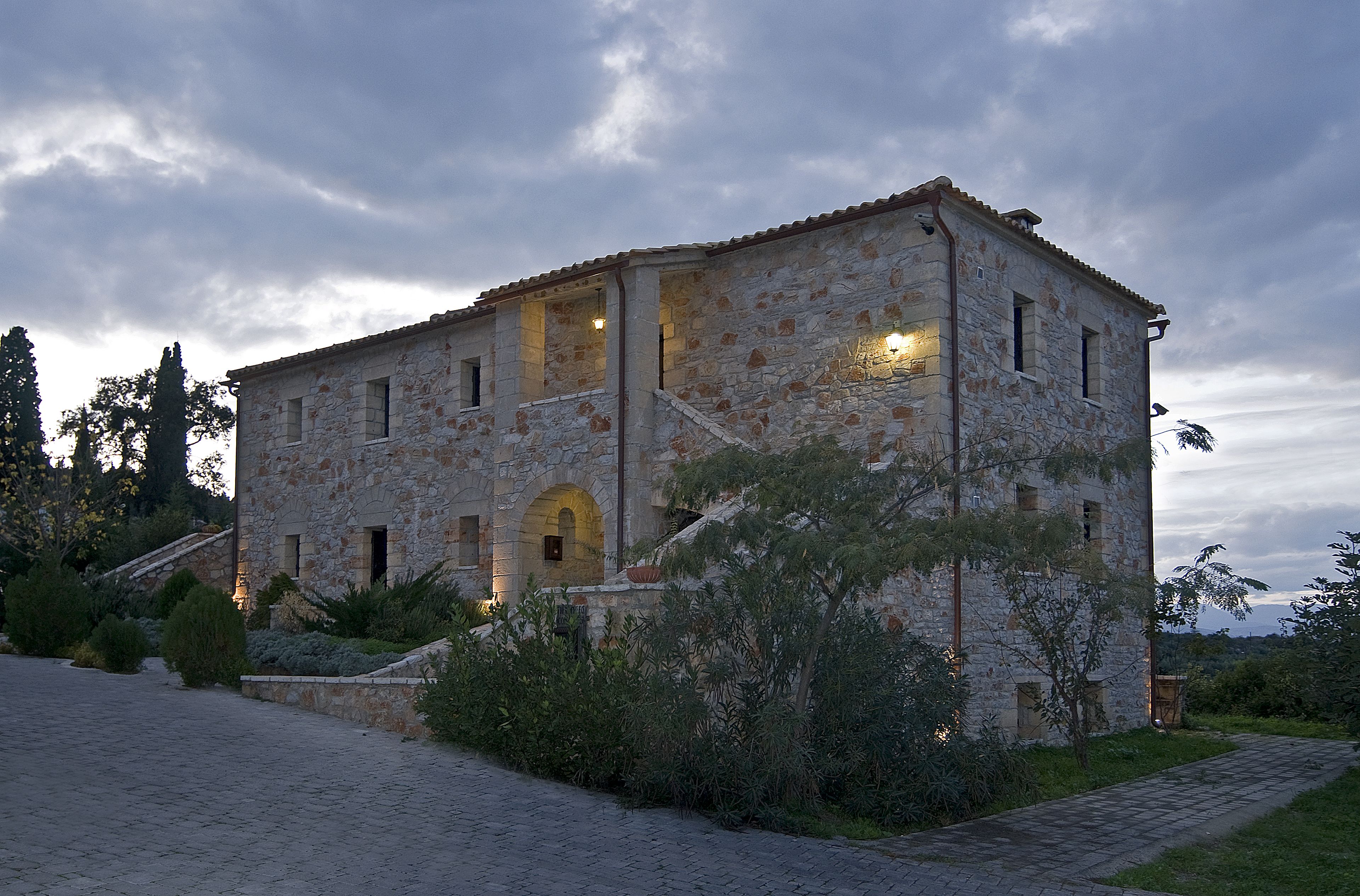 A stone building with a tiled roof, arched windows, and a paved pathway leading to it.