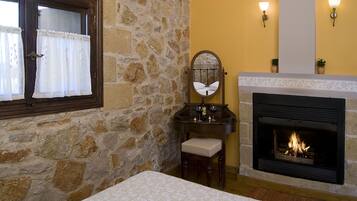 A bedroom with a stone wall, a fireplace, a bed, a nightstand, a mirror, and a window with curtains.