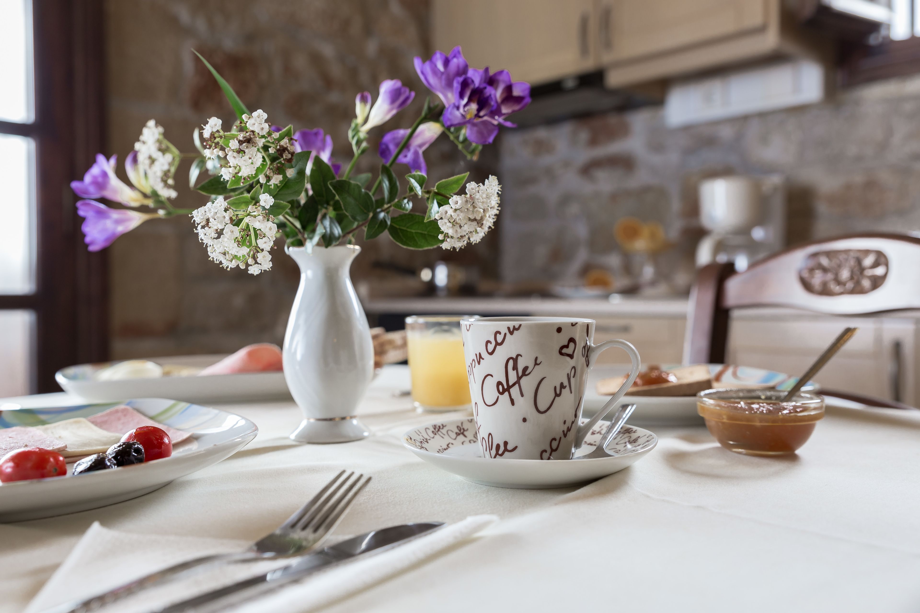 A breakfast table with a coffee cup, a vase of flowers, and a plate of food.