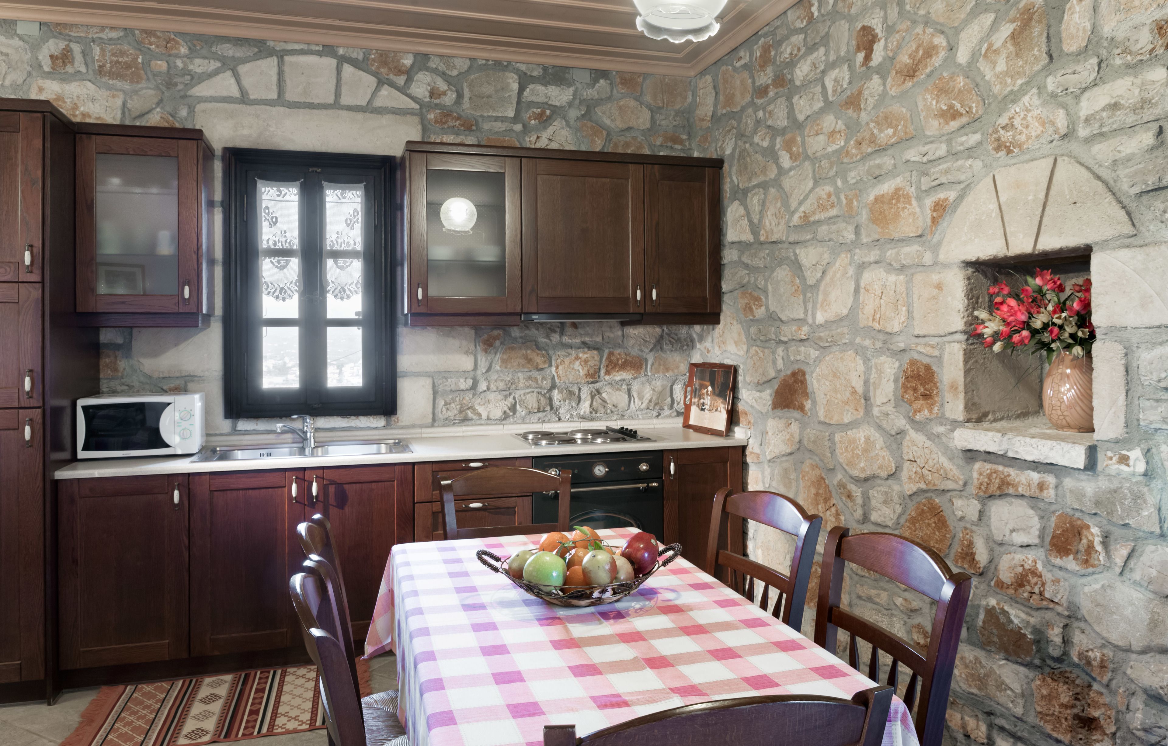 A stone-walled kitchen with wooden cabinets, a microwave, and a dining table with chairs.