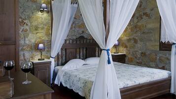A four-poster bed with white curtains, a wooden nightstand with a lamp, and a stone wall backdrop.