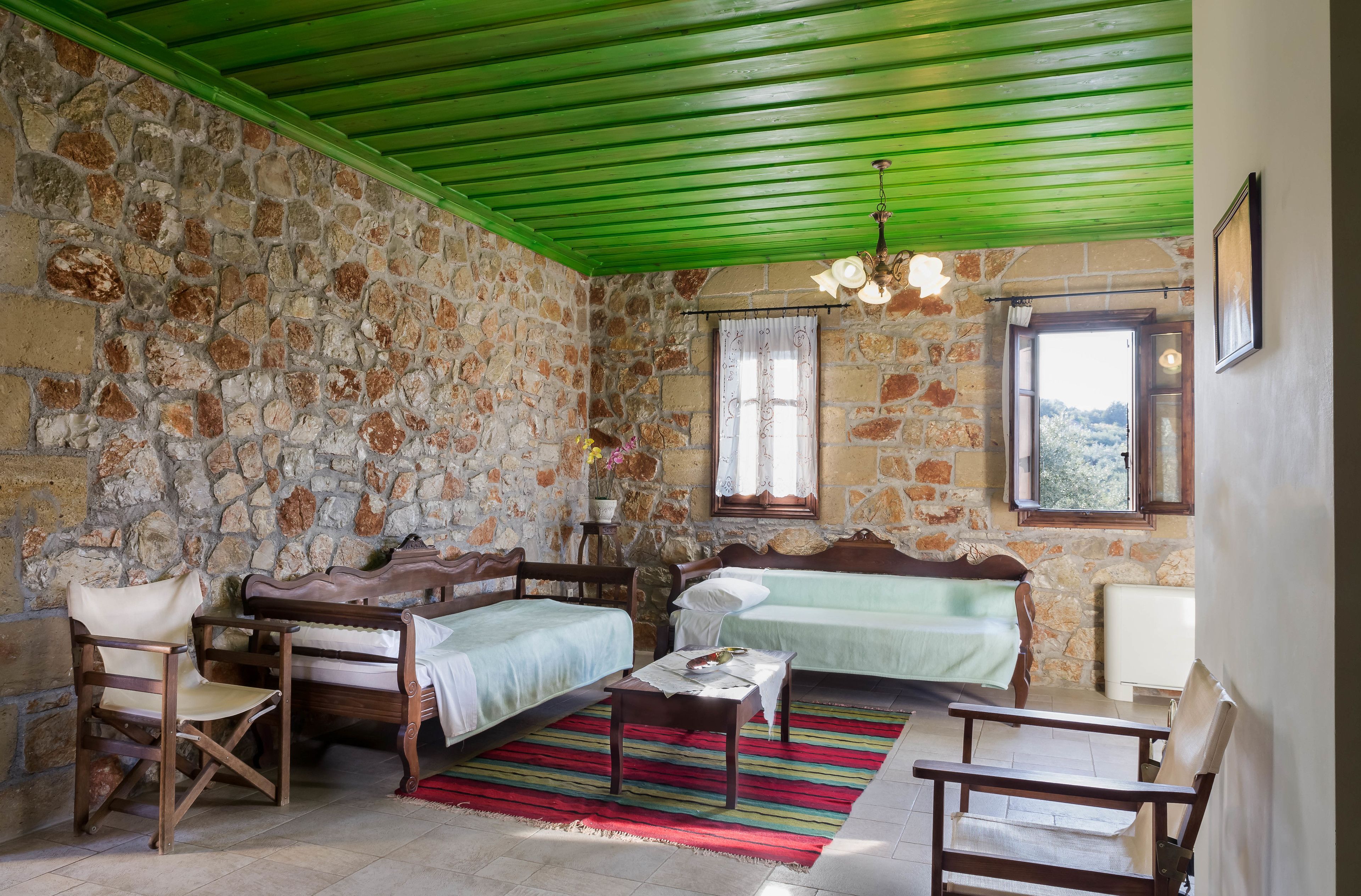 A room with stone walls, two beds, a wooden chair, a table, and a green ceiling.