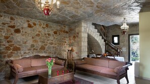 Una habitación de paredes de piedra con dos sofás a rayas, una mesa de centro de madera y una araña.