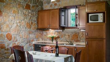 Una cocina de paredes de piedra con armarios de madera, una mesa de comedor para dos personas y una botella de vino.
