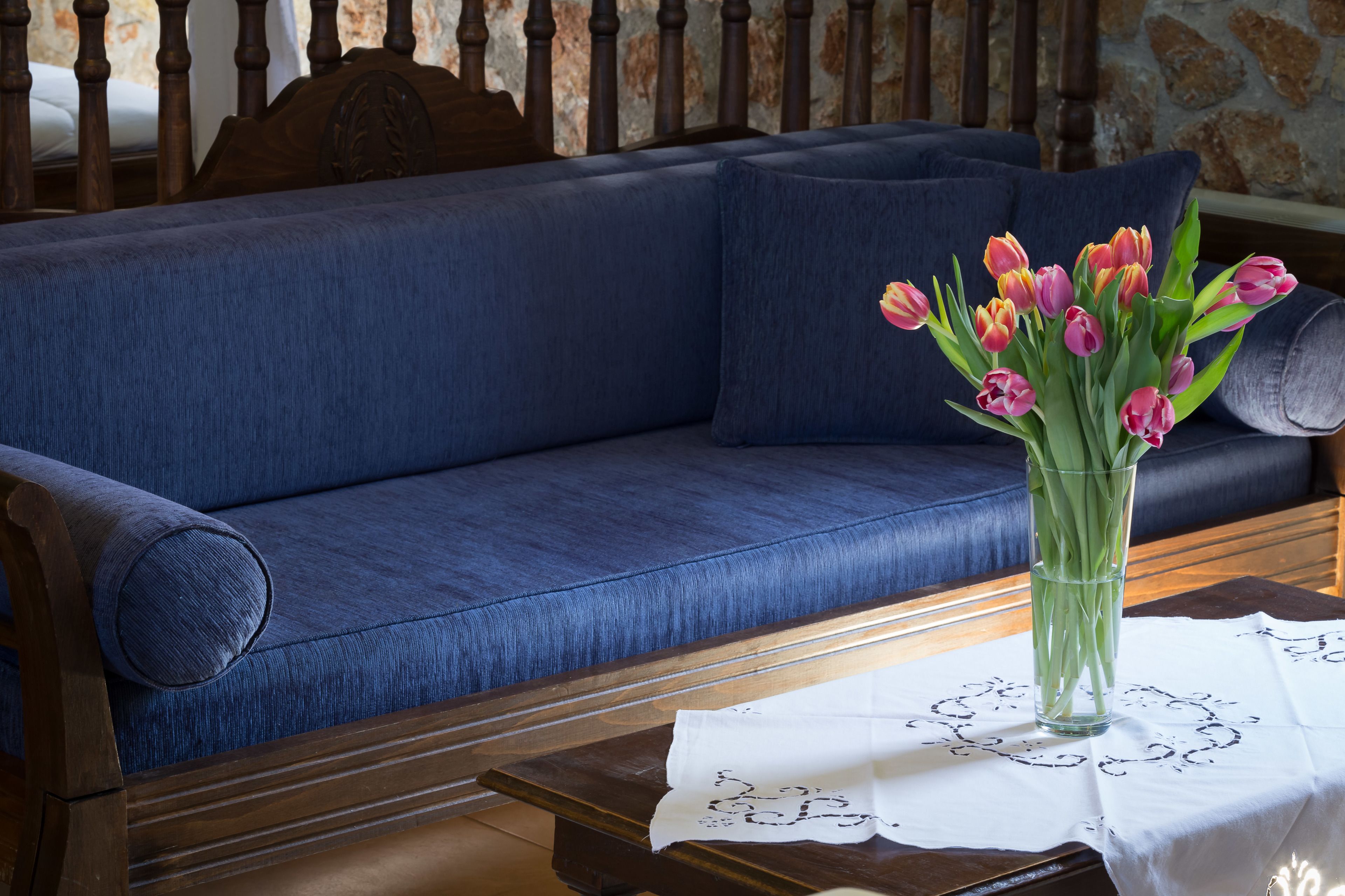 A blue sofa with a vase of pink and orange tulips on a table with a white cloth.