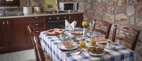 A breakfast table set with plates, bowls, and cups, a toaster, and a microwave on a kitchen counter with stone walls.