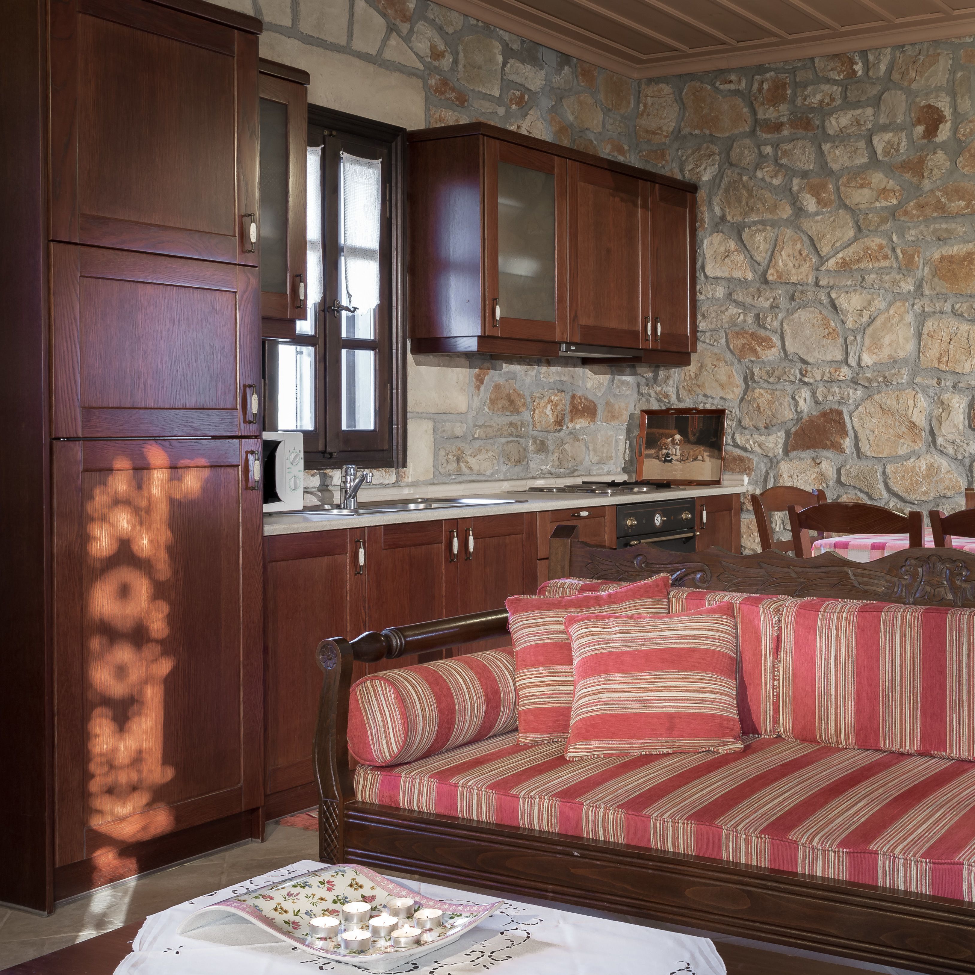 A cozy kitchen with wooden cabinets, a stone wall, and a dining area with a sofa and chairs.