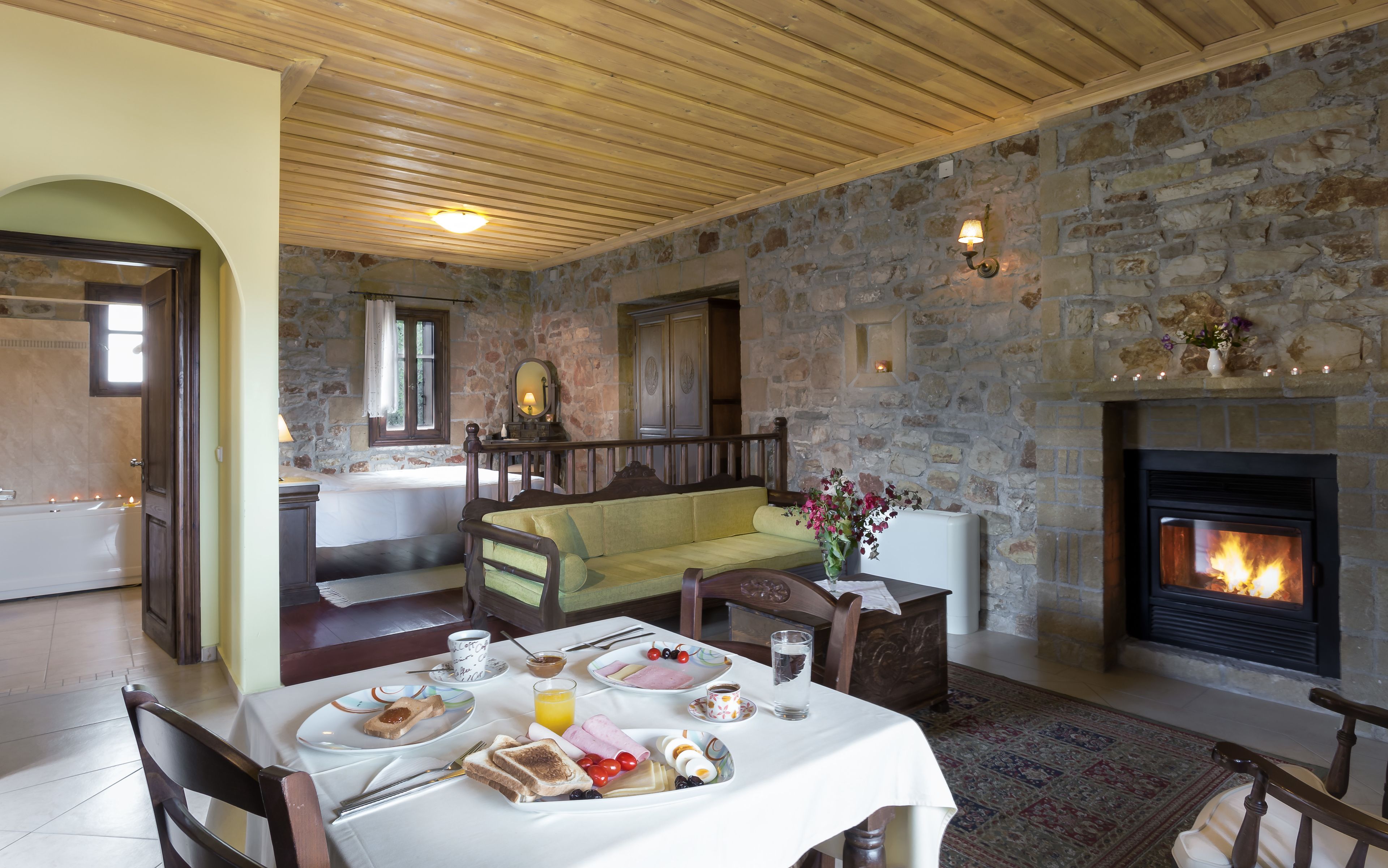A cozy room with a stone wall, a fireplace, a dining table set with breakfast, and a bench.