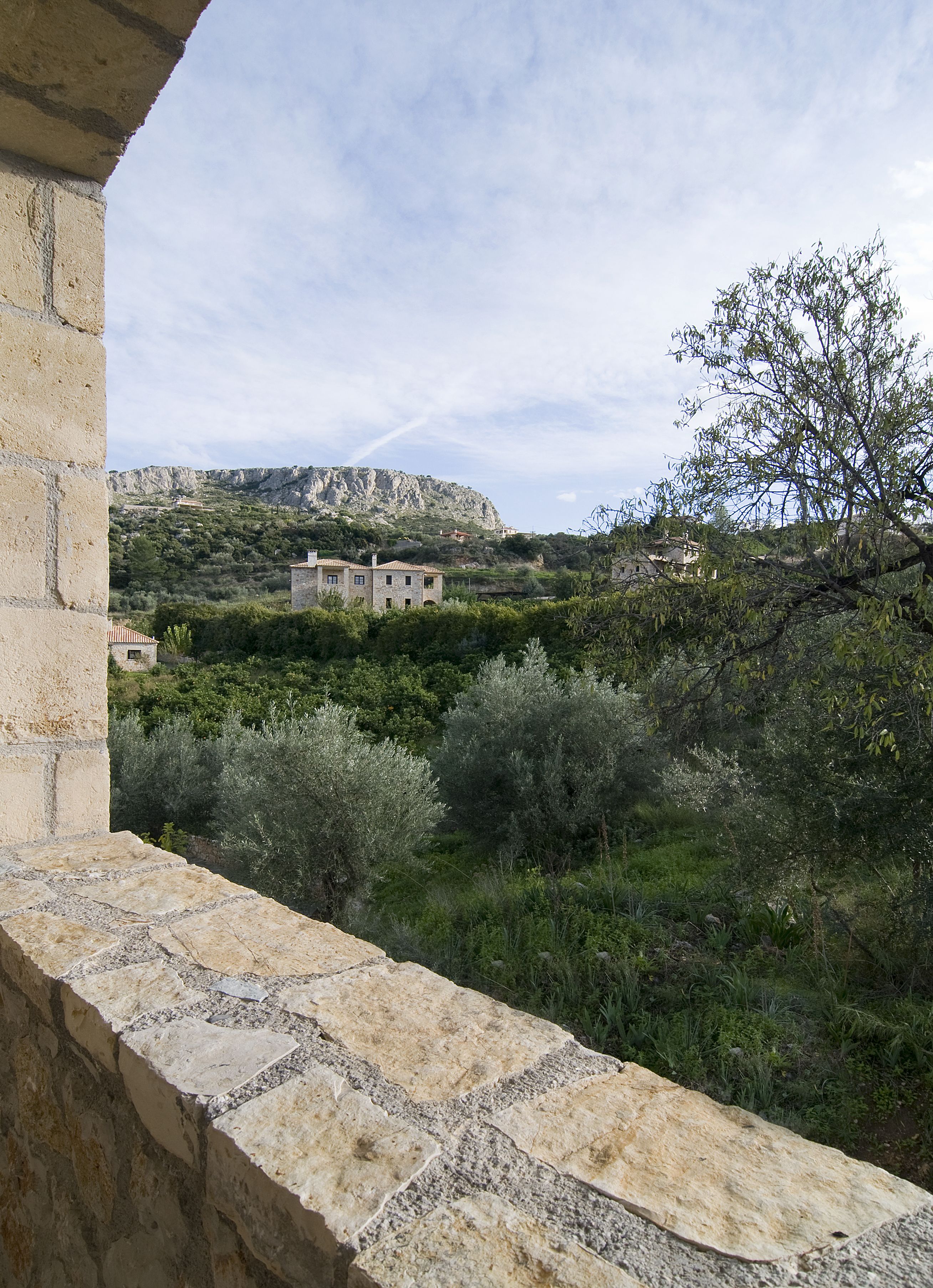 A stone balcony overlooking a rural landscape with a stone building and trees.