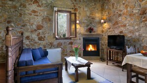 Una habitación con paredes de piedra, una chimenea, un sofá, una mesa con un jarrón de flores y un televisor sobre un mueble.