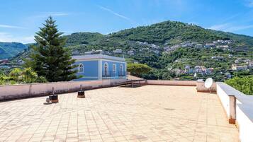 A rooftop terrace with a view of a hillside village, a blue building, and a satellite dish.