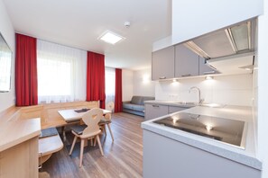 A modern kitchen with a built-in stove and a dining area with a wooden table and chairs. - Mountain Residence Montana (Valle di Casies)