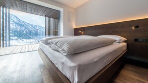A modern bedroom with a large bed, wooden flooring, a view of mountains, and a wooden ceiling. - Mountain Residence Montana (Valle di Casies)