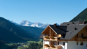 A wooden chalet with a balcony, set against a backdrop of mountains and a clear sky. - Mountain Residence Montana (Valle di Casies)