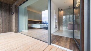 A modern interior with a wooden floor, a glass door leading to a bedroom, and a shower area with a glass enclosure. - Mountain Residence Montana (Valle di Casies)