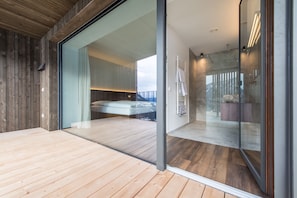Um interior moderno com piso de madeira, porta de vidro que dá para um quarto e área de chuveiro com divisória de vidro.
