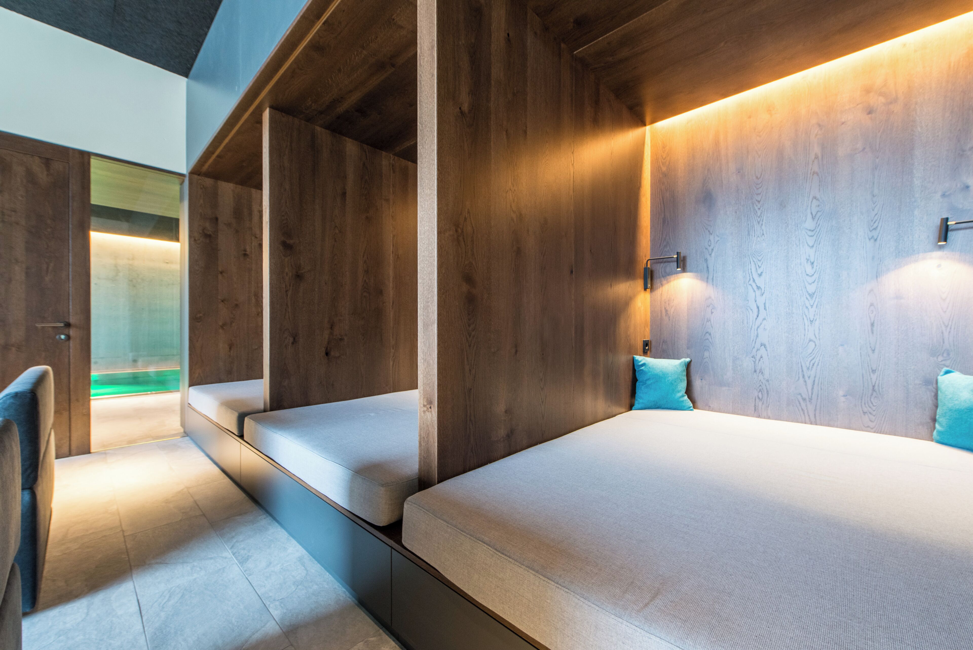Una habitación moderna con camas empotradas de madera, un banco y una puerta de vidrio que da a un área verde.