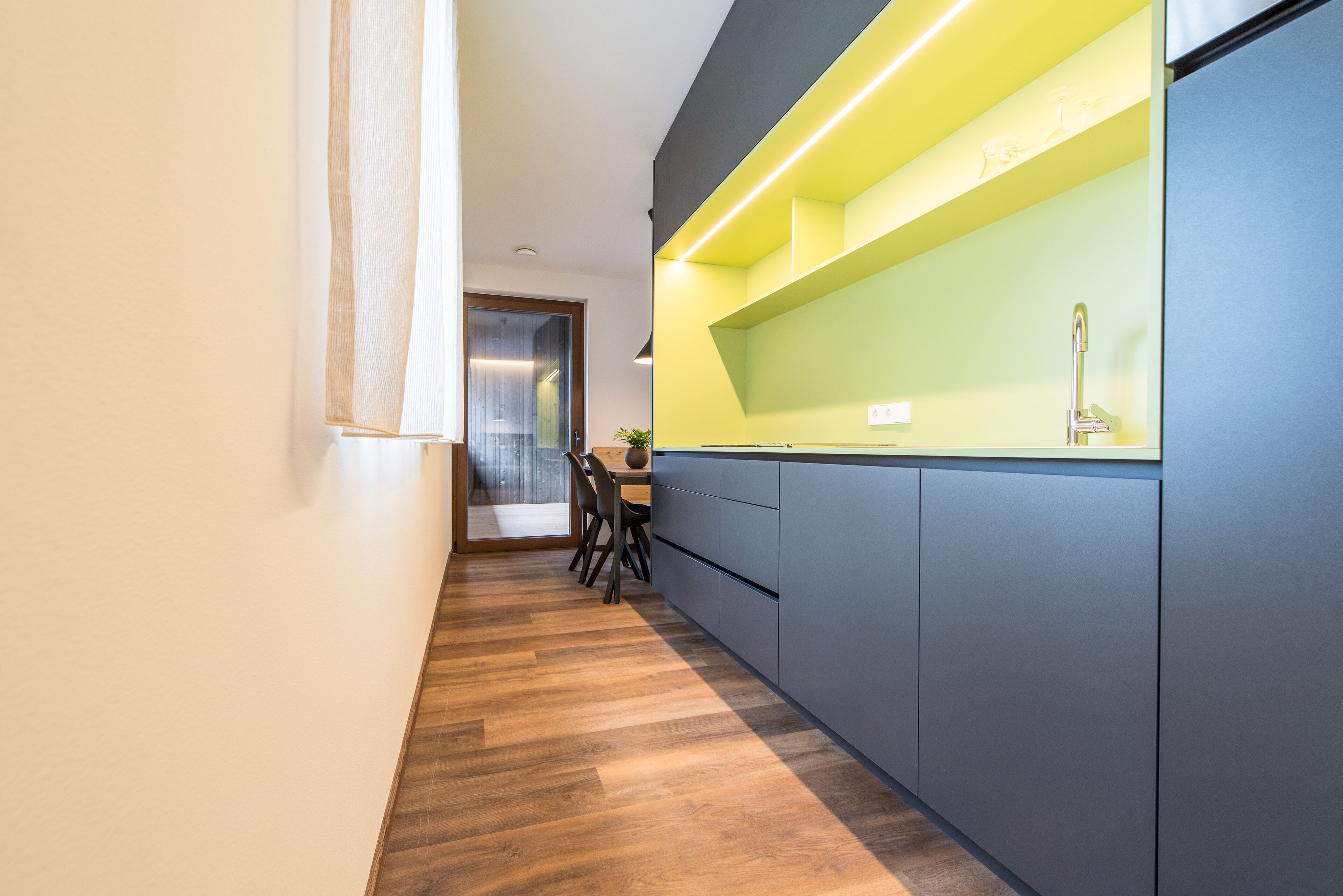 A modern kitchen with a wooden floor, a dining area with chairs, and a built-in sink.