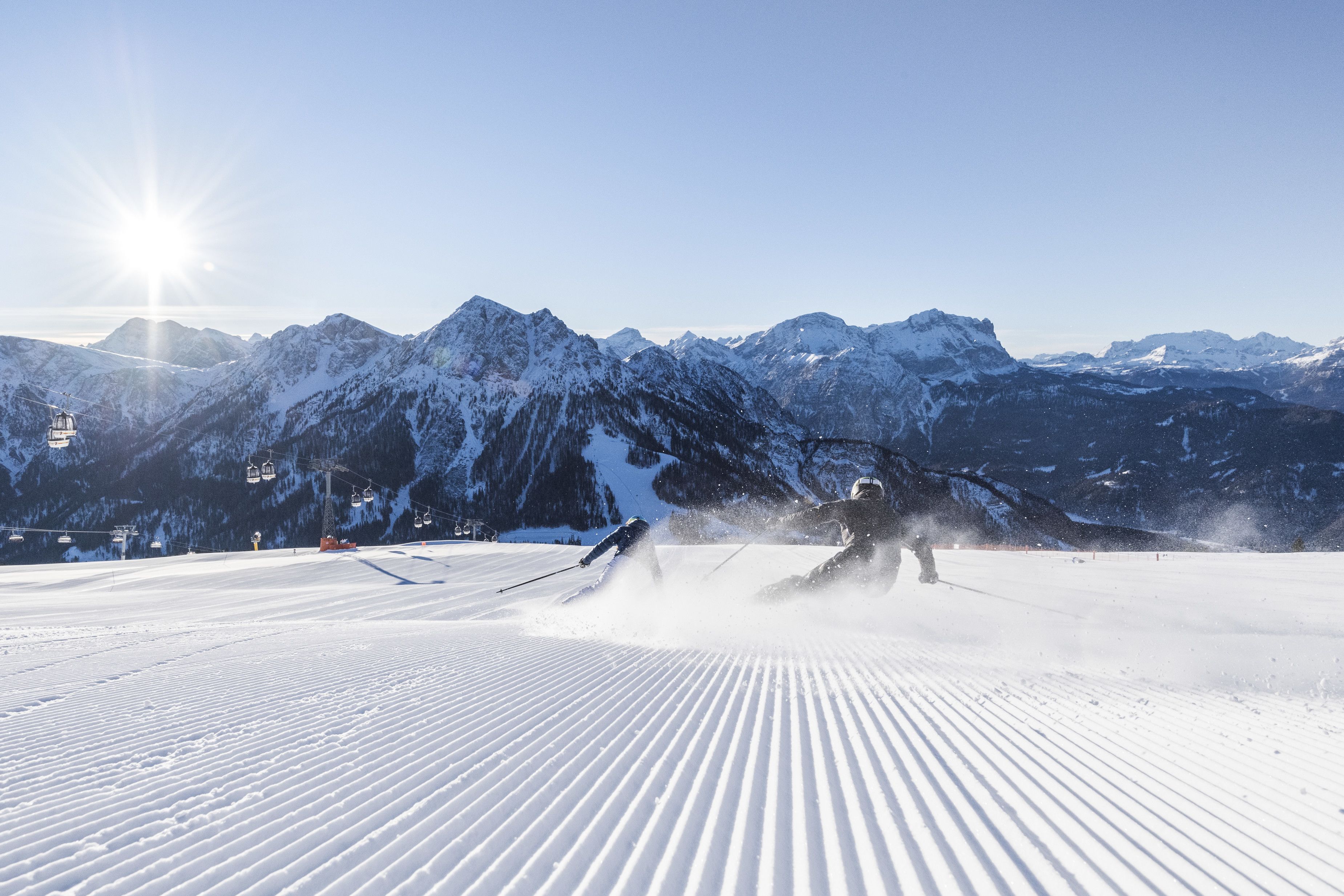 A ski slope with groomed snow, ski lifts, and a mountainous backdrop.