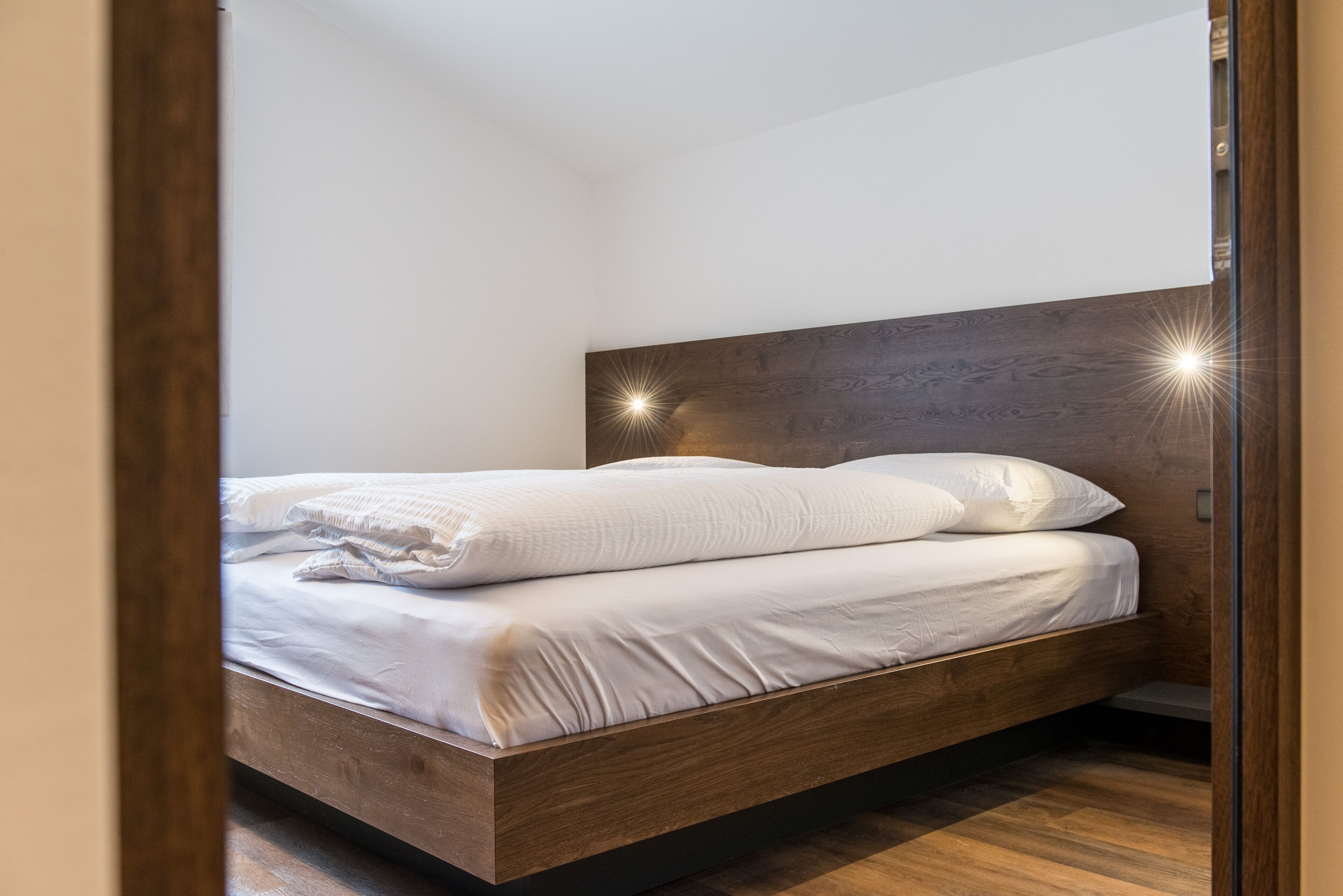 Een moderne slaapkamer met een houten hoofdbord, een opgemaakt bed met witte lakens en een houten vloer.