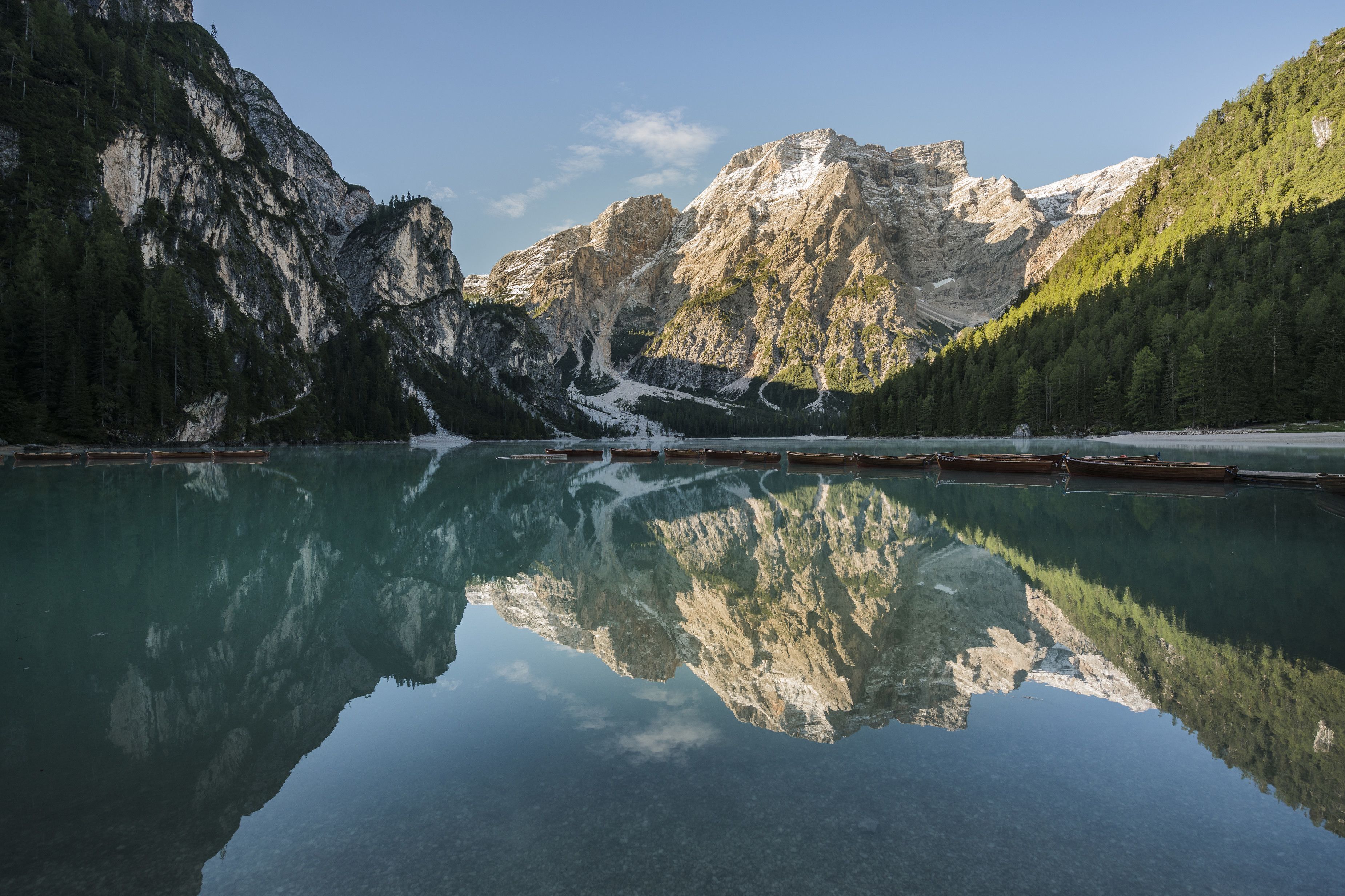 A mountain lake with clear reflections of the surrounding peaks and forested slopes.