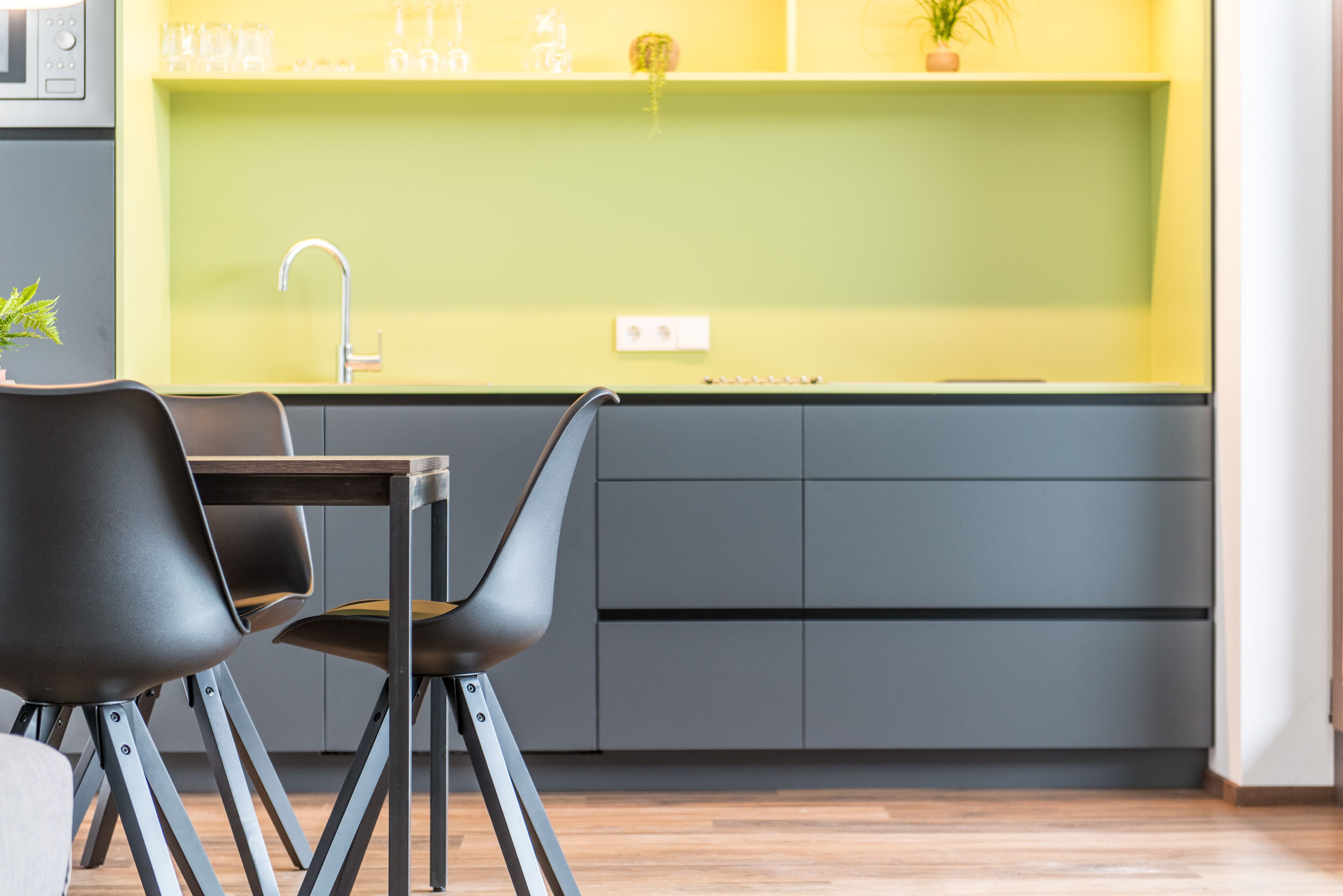 A modern kitchen with a green countertop, grey cabinets, and a black chair.