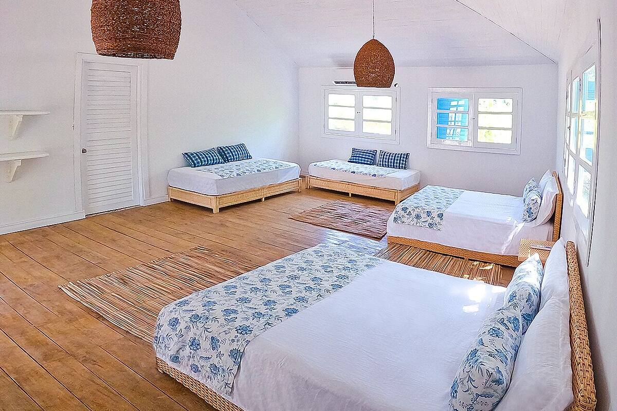 Ein Zimmer mit drei Betten, Holzboden und einem großen Fenster.