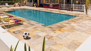 Ein Poolbereich mit Liegestühlen, einer Flagge und einem Gebäude mit der Aufschrift 'COLOMBIA'.
