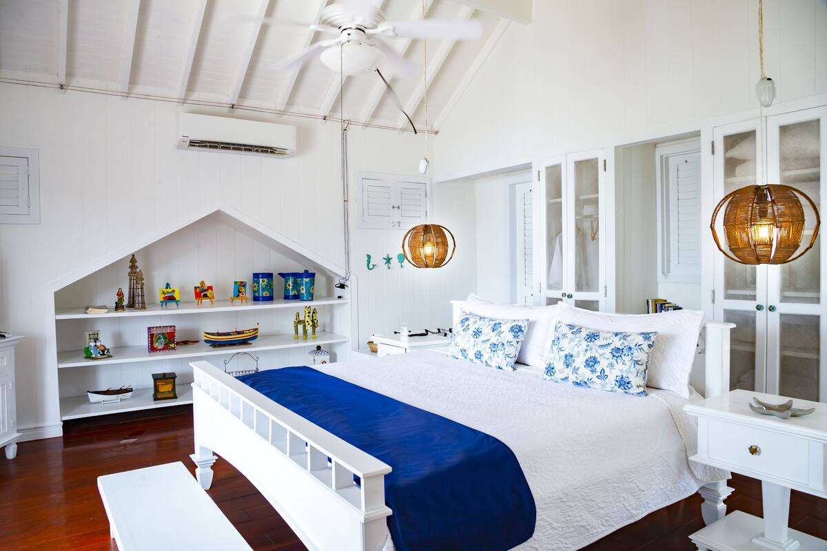 Ein Schlafzimmer mit einem weißen Bett, blauer Bettwäsche, weißen Möbeln und einem Deckenventilator.
