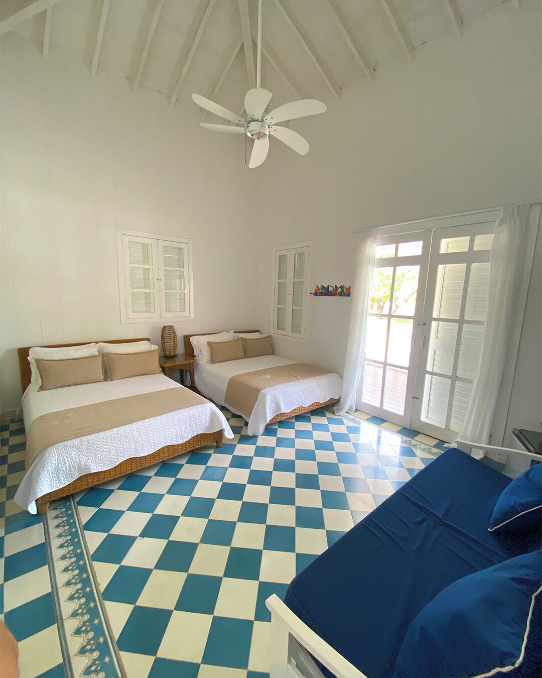 A room with two beds, a ceiling fan, and a checkered floor.