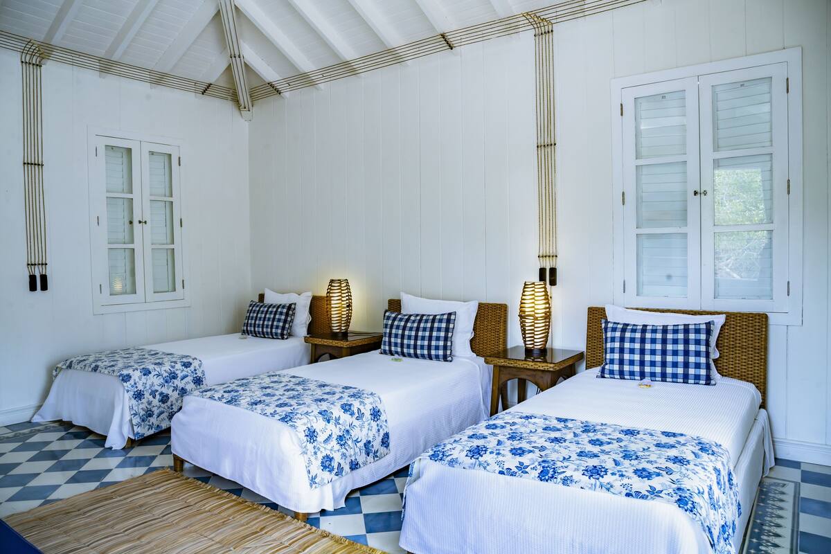 Ein Zimmer mit drei Betten, jeweils mit weiß-blauer Blumenbettwäsche, Holzkopfteilen und Nachttischlampen.