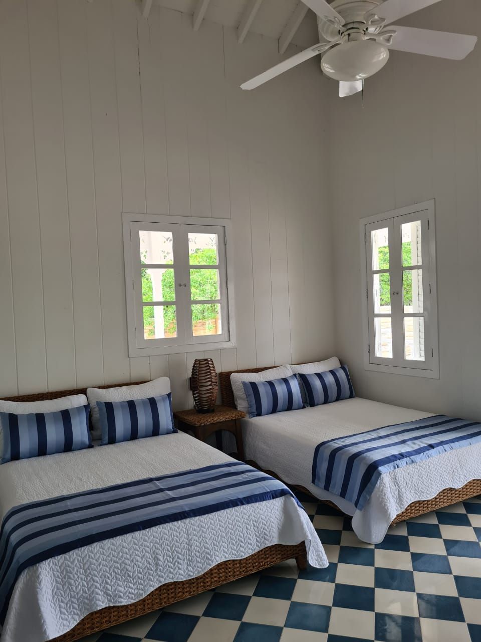 Habitación con dos camas, ventilador de techo y ventanas con vistas a zonas verdes.