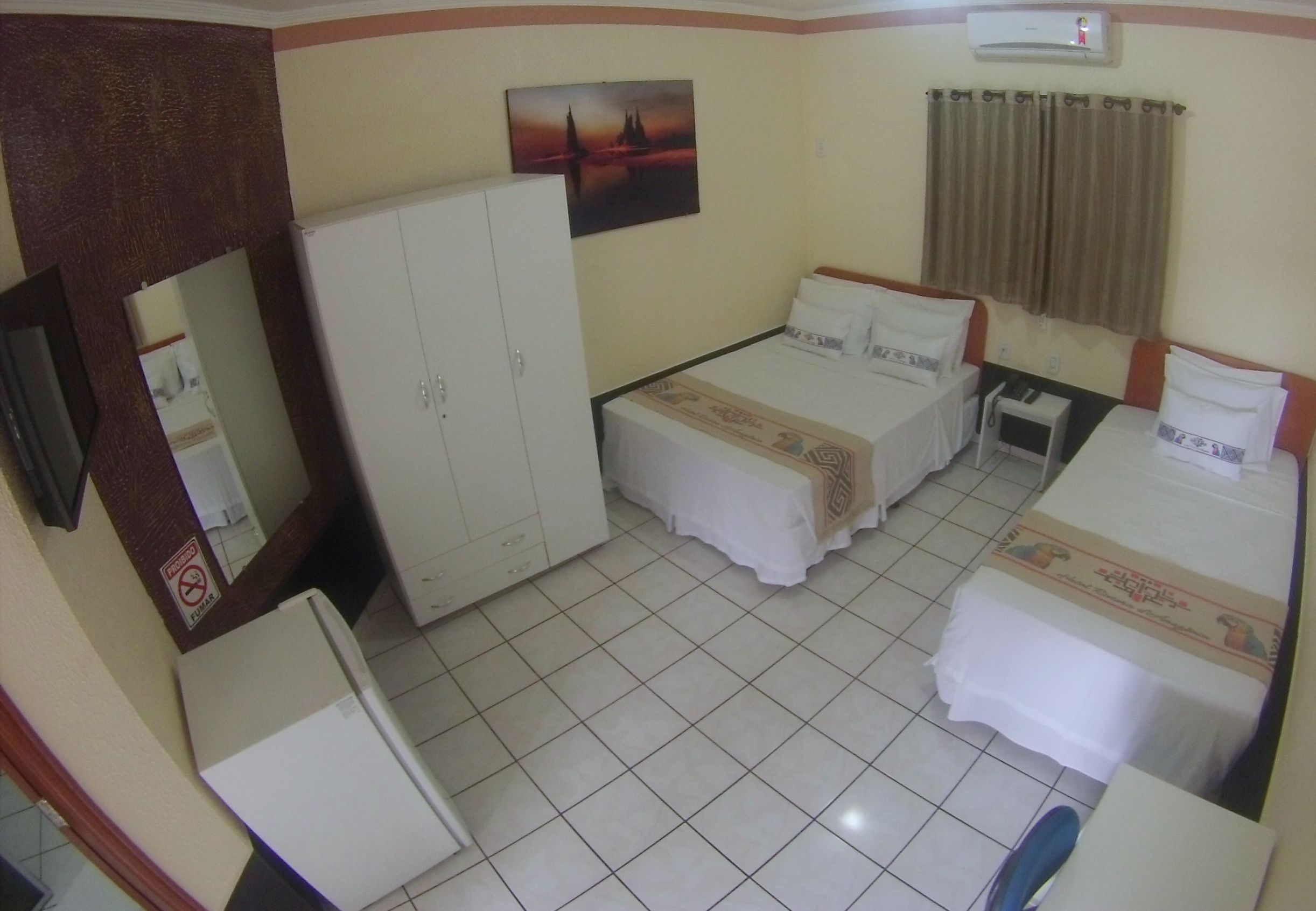 A hotel room with two beds, a wardrobe, a mirror, a flat-screen TV, and a ceiling fan.