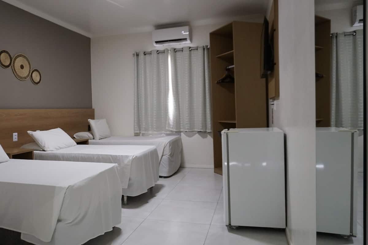 A hotel room with two beds, a wardrobe, a refrigerator, and an air conditioning unit.