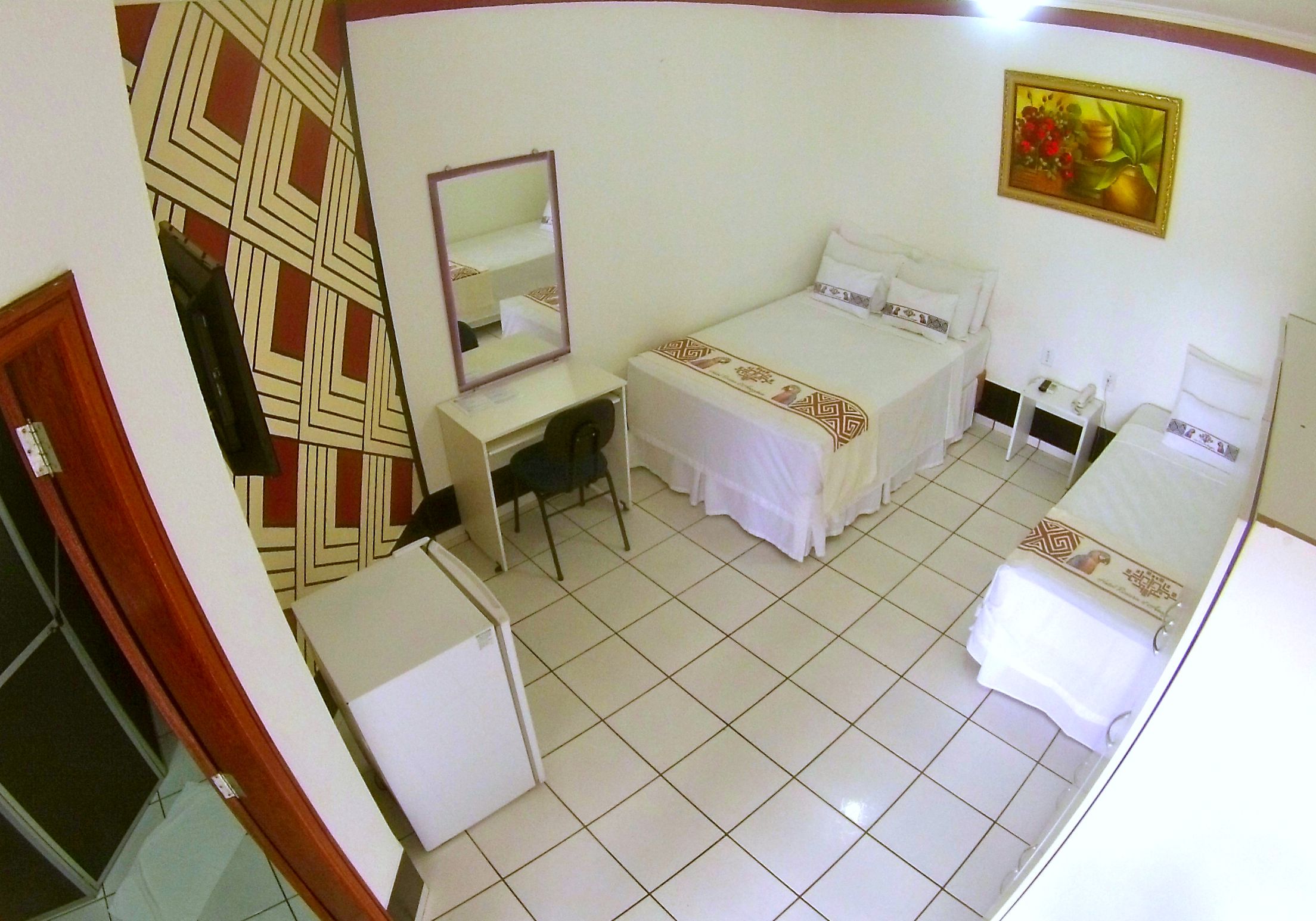 A hotel room with two beds, a desk, a chair, a small table, and a mirror.