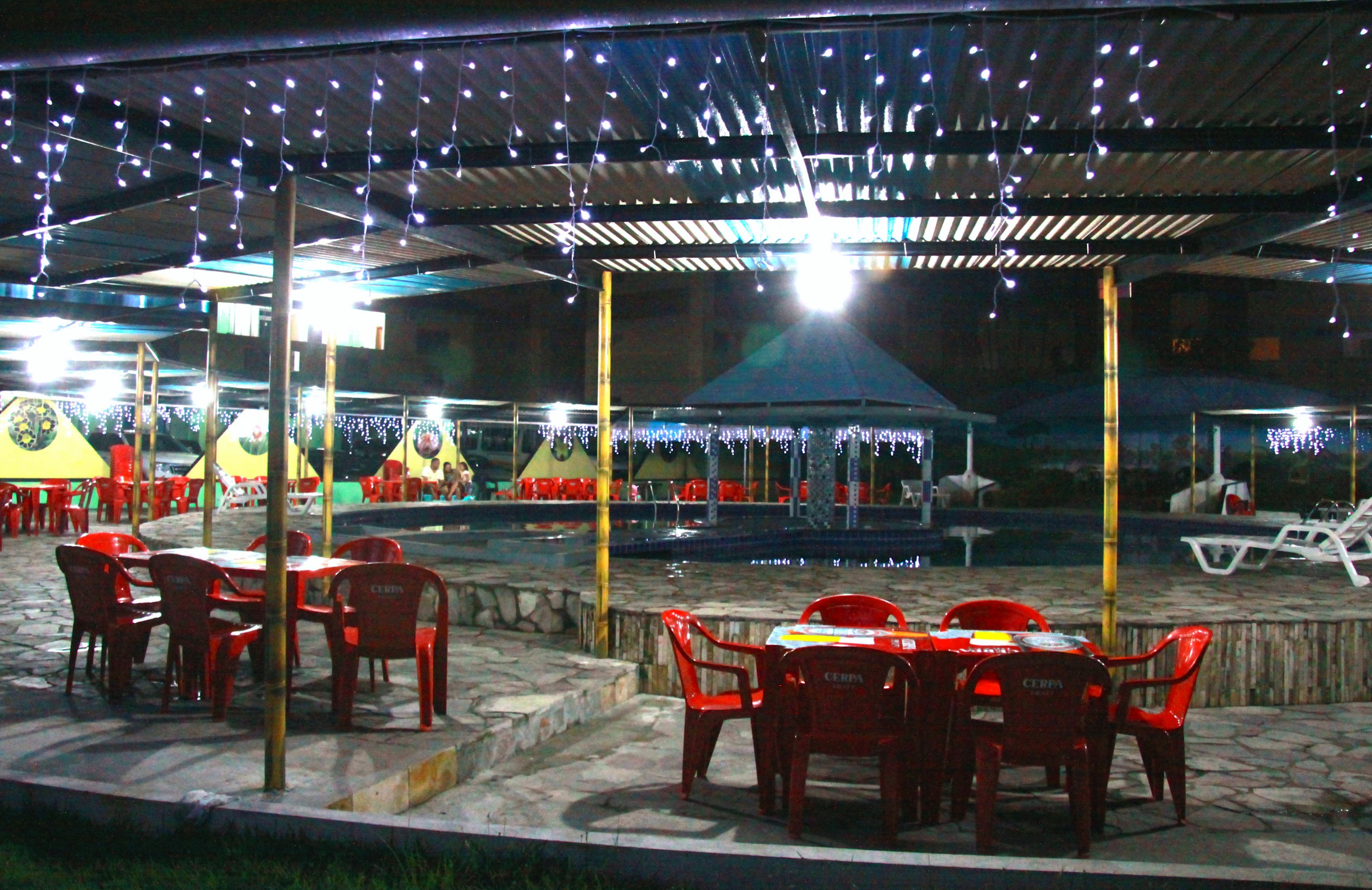 Un patio al aire libre con mesas, sillas, piscina y luces colgantes.