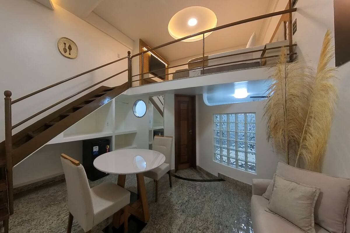A spacious living area with a high ceiling, a staircase, a round dining table, and a sofa.