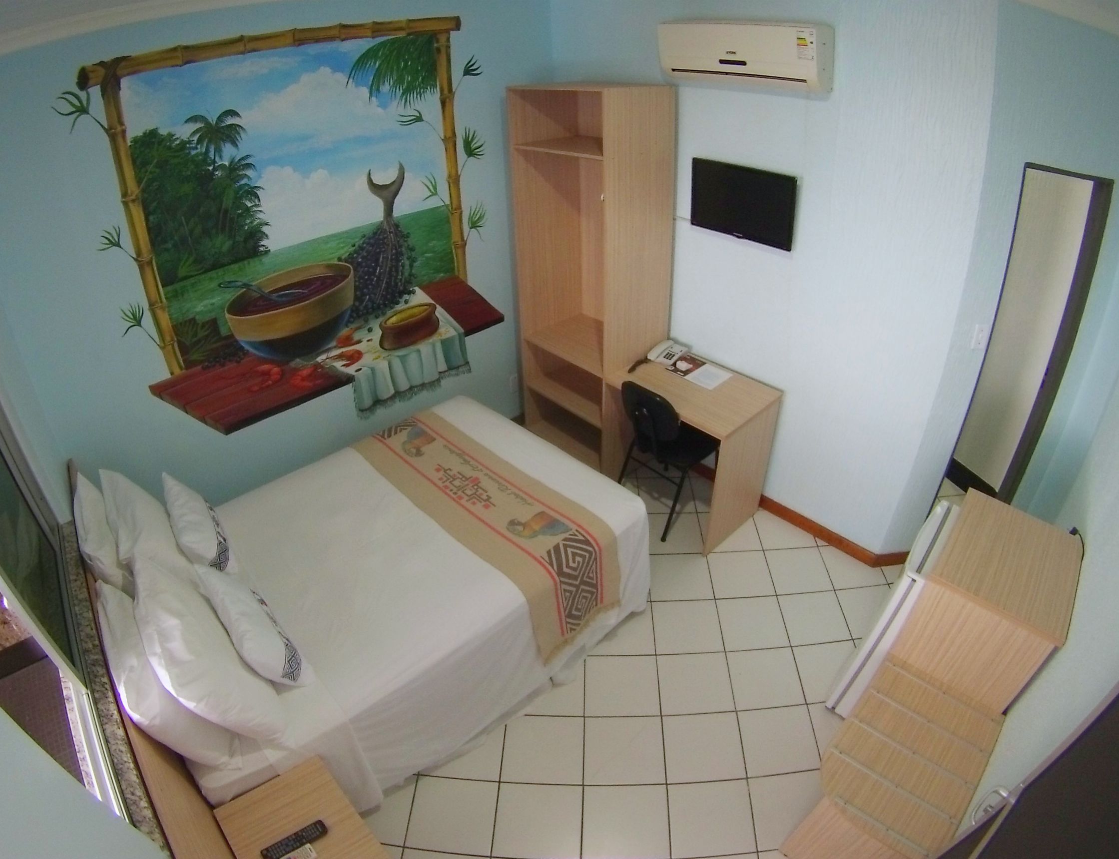 Ein Hotelzimmer mit Bett, Schreibtisch, Stuhl, Kleiderschrank, Fernseher und Spiegel.