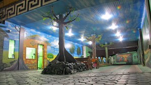 An indoor space with a tiled floor, a mural of a tree, and a building with a green door. - Hotel Riviera D'Amazonia (Ananindeua)