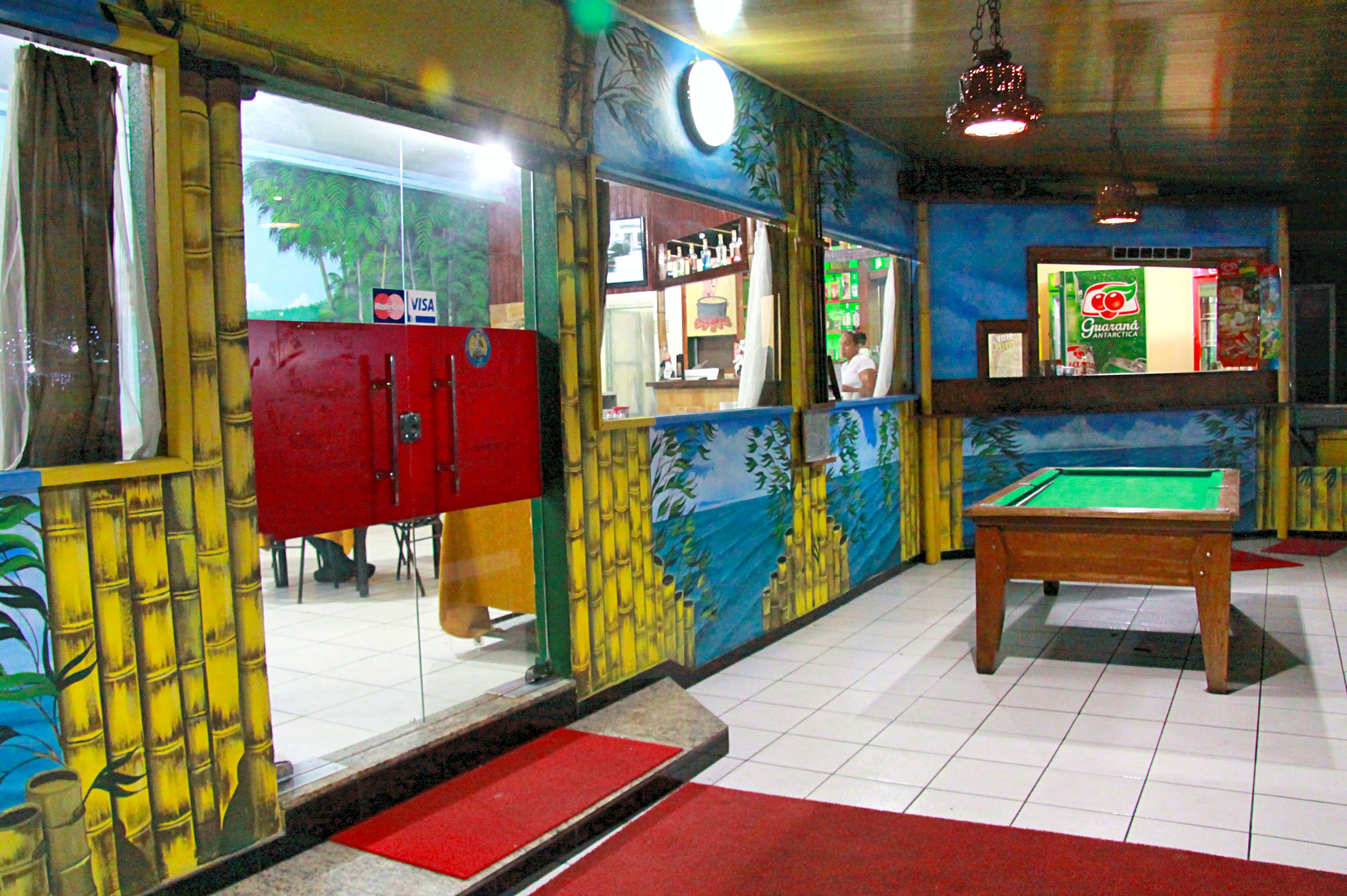 Une table de billard dans une pièce ornée d’une fresque représentant des bambous et des palmiers, avec un buffet rouge et un comptoir où sont exposées des boissons.