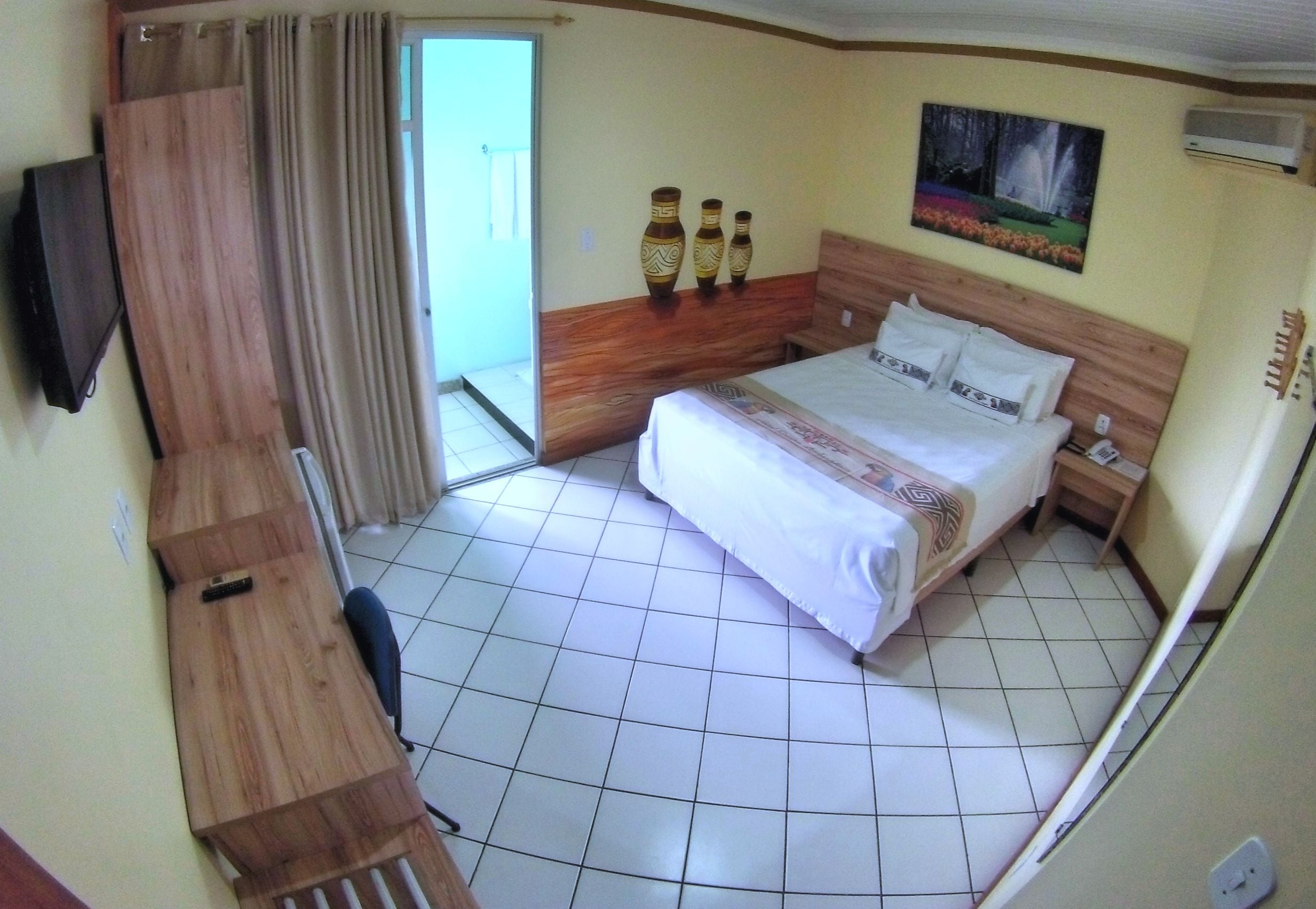 Habitación de hotel con cama, escritorio, silla, televisión y un cuadro en la pared.