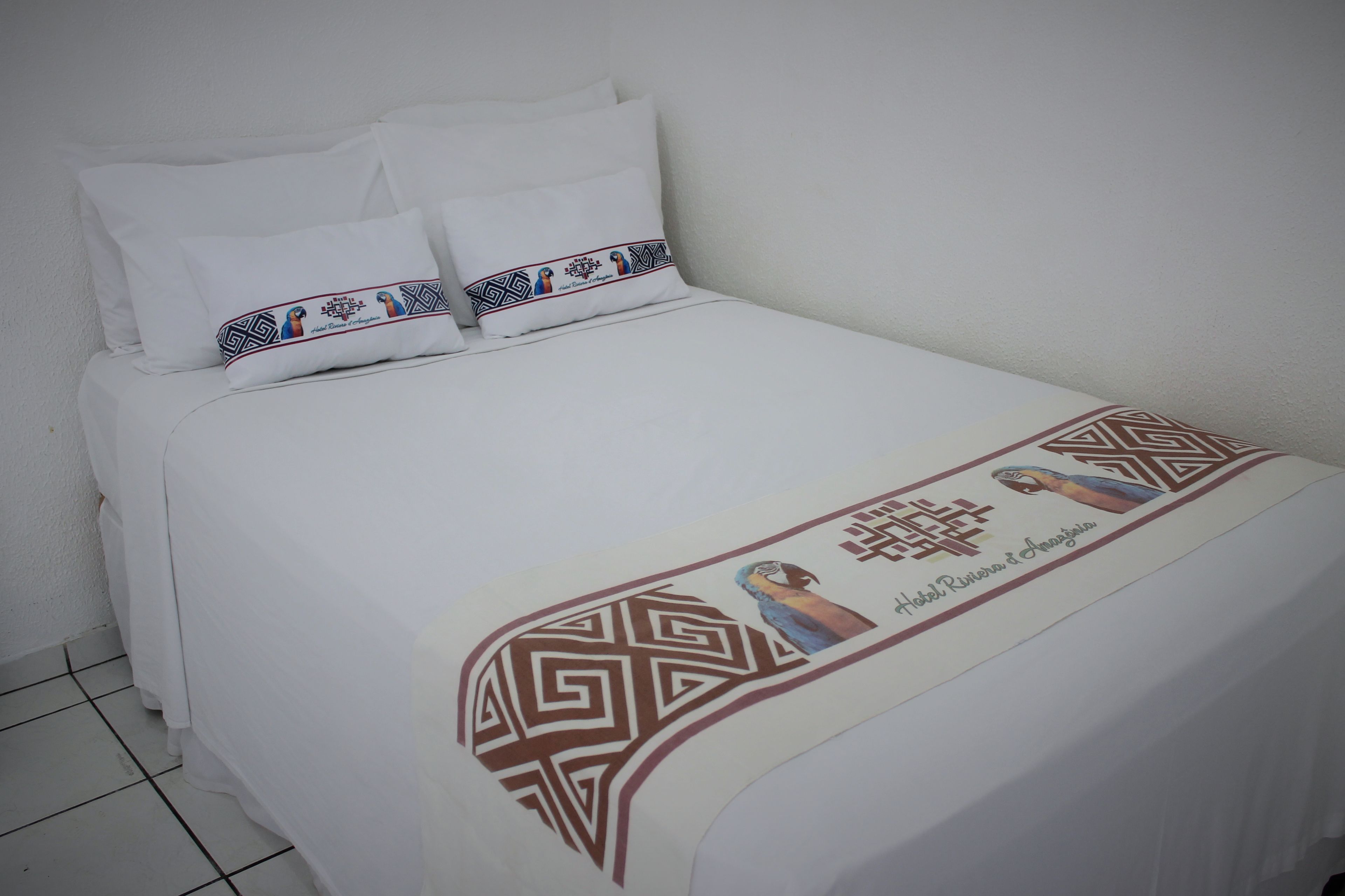 Una cama bien tendida con sábanas blancas y un cojín decorativo con motivos culturales.