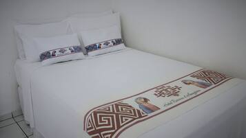 Una cama bien tendida con sábanas blancas y un cojín decorativo con motivos culturales.