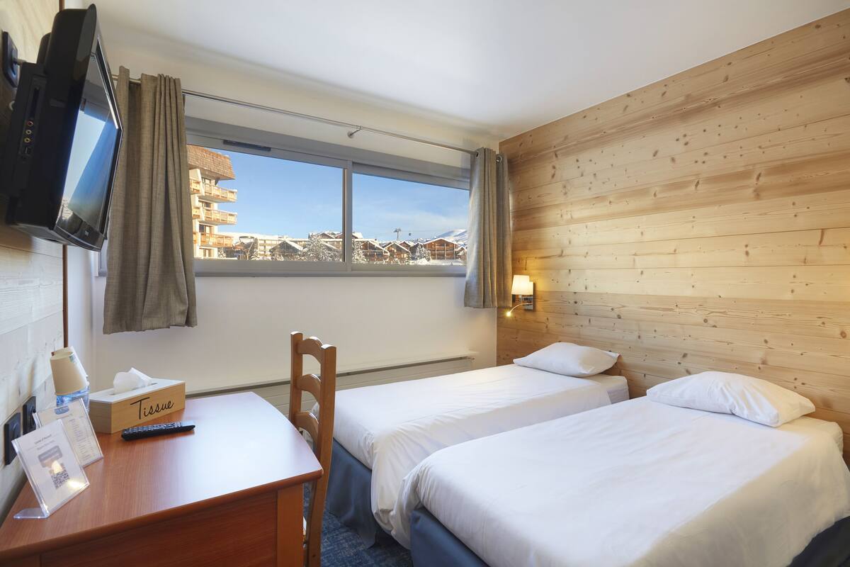 A hotel room with two beds, a desk with a tissue box, a remote control, and a TV mounted on the wall.