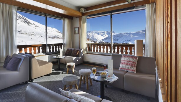 A cozy room with a balcony, large windows, and a view of snow-covered mountains.