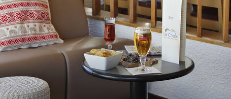 Et hyggeligt opholdsområde med en polstret sofa, et lille rundt bord med snacks, et glas rødvin og et glas øl.